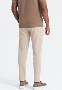 Pantalon beige en mélange de coton avec une coupe fuselée, doté d'un tissu texturé et d'une ceinture élastique. Porté avec des chaussures marron à enfiler.
