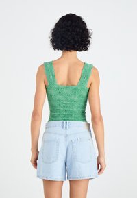 Zeleni pleteni top s teksturiranim vzorcem in širokimi naramnicami, v kombinaciji s svetlo modrimi jeans kratkimi hlačami, ki imajo dve zadnji žep.