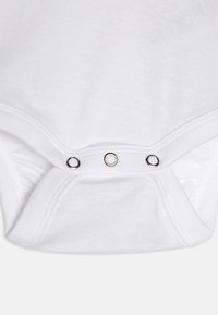 Weißer Baumwoll-Bodysuit mit Druckknöpfen im Schritt, der eine glatte Textur und eine figurbetonte Passform aufweist. Die Nähte sind ordentlich verarbeitet.