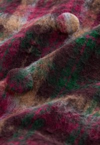 Kangastooted, millel on värvikas, karvane pind punaste, roheliste ja pruunide toonide segus, ning kangasse on sisse õmmeldud tekstuuriga ümmargused nööbid.