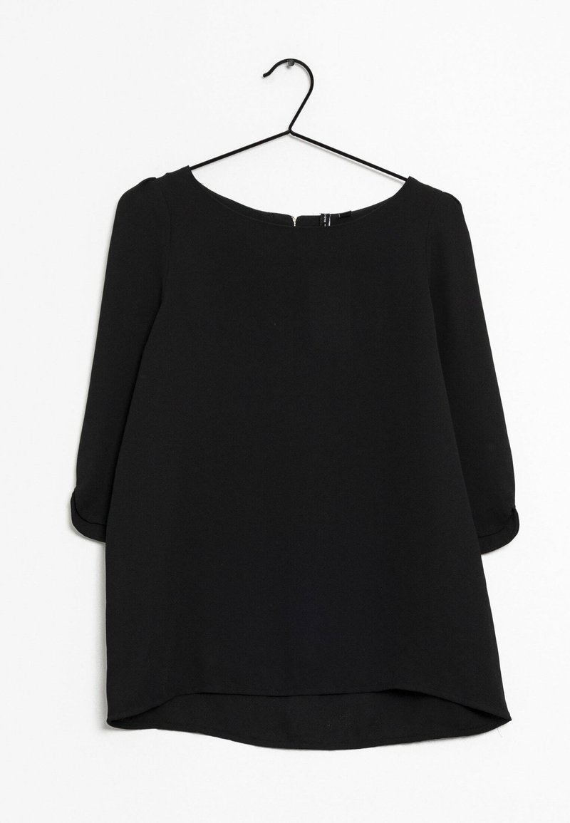 Blouse noire à manches longues avec col rond et ourlet légèrement incurvé, suspendue sur un cintre métallique noir sur fond blanc.