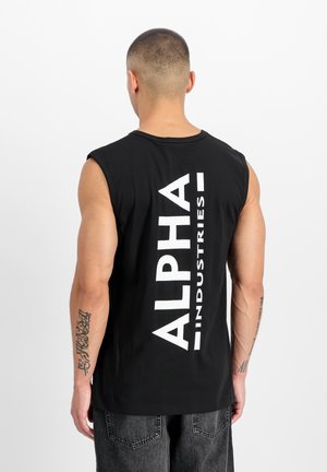 Man with short hair wearing black sleeveless shirt with "ALPHA INDUSTRIES" text on back, paired with dark jeans, facing away.