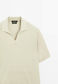 Lichtbeige polo shirt met korte mouwen en V-hals, gemaakt van soepel katoen. Voorzien van een geribbelde kraag en naadloze schouders.