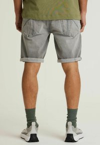 Grå denimshorts med oprullede kanter, der har to baglommer. Båret med grønne sokker og lyse sneakers, set fra ryggen.
