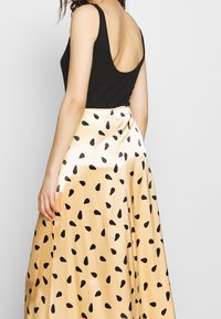 Haut sans manches noir associé à une jupe en satin doré ornée d'un motif de gouttes noires, mettant en valeur un contraste de textures et de designs.