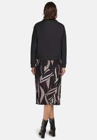 Zwarte sweatshirt met ronde hals, gecombineerd met een geprinte rok tot de knie met een geometrisch abstract patroon in aardse tinten.