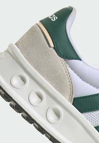 Sneaker vert et blanc en daim et cuir synthétique, semelle intermédiaire blanche texturée avec des découpes circulaires, et rayures vertes contrastantes.