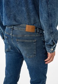 Vaqueros de mezclilla azul oscuro con un ajuste slim, que cuentan con bolsillos traseros, un parche de cuero en la cintura y detalles de costura en contraste.