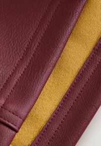 Gros plan sur un cuir bordeaux avec des coutures visibles à côté d'un tissu en daim jaune moutarde.