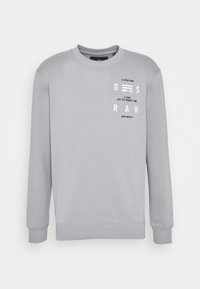 Sudadera gris claro con cuello y puños acanalados, con texto impreso en blanco y diseños gráficos en la parte frontal. Textura de tela suave.