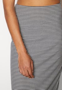 Svartvitt hundtandsmönstrat figurnära kjol med en slät textur, midja vid den naturliga midjan och smal fåll.