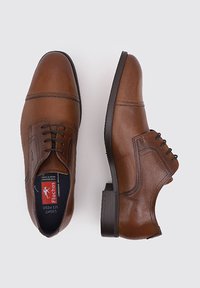 Zapatos de vestir de cuero marrón con una textura suave; costuras definidas, diseño de cordones y un tacón ligeramente elevado. Incluye el logo de la marca en el interior.