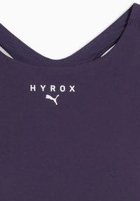 Lähedalt vaade lillast sporditopist, millel on valge "HYROX" tekst ja Puma logo kaelaesise all, võrgukangast äärisega.