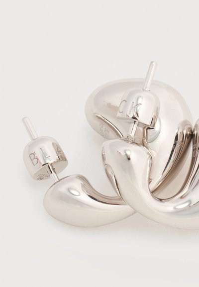 Καμπυλωτά, γυαλιστερά ασημένια μεταλλικά σκουλαρίκια με λαξευμένες πίσω πλευρές που φέρουν τα γράμματα «CK» στο ένα και «BLA» στο άλλο.