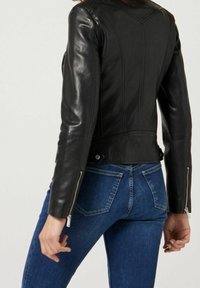 Svart läderjacka med figursydd design, långa ärmar och synliga sömnadsdetaljer. Har dragkedjor på ärmsluten och en kortad nederkant.