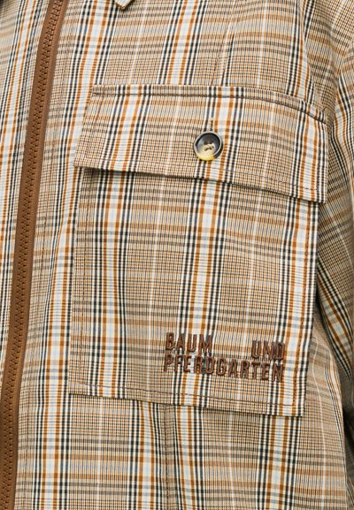 Καρό πουκάμισο σε καφέ και μπεζ αποχρώσεις με πλήρες φερμουάρ, τσέπη στο στήθος και κεντημένο κείμενο. Διαθέτει κλείσιμο με κουμπιά και υφασμάτινη υφή.