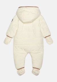 Combinaison de neige pour bébé de couleur crème, rembourrée, avec capuche attachée, moufles et chaussons, vue de dos sur un fond blanc.