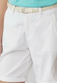 Weiße Baumwollshorts mit umgeschlagenem Saum, ausgestattet mit einem geflochtenen cremefarbenen Gürtel und einer silbernen Schnalle. Strukturiertes Material und klarer Schnitt.