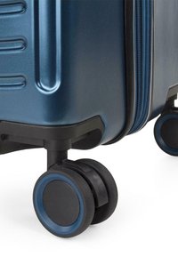 Maleta rígida de plástico azul oscuro con superficie texturizada, que cuenta con cierre de cremallera y ruedas negras con acentos azules.