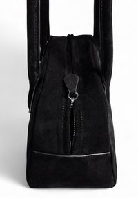 Melnas zamšādas soma ar taisnstūra formu, divām rokturiem un ar rāvējslēdzēju aizveramu vāku, kas aprīkota ar teksturētu vilkšanas cilpu un sudraba aparatūru.