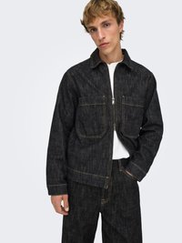 Veste en denim foncé avec surpiqûres jaunes contrastantes, deux poches poitrine, fermeture éclair et coupe décontractée, associée à un pantalon en denim foncé assorti.