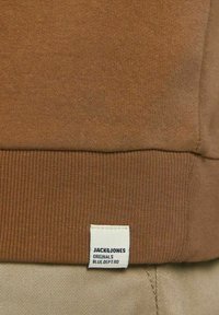 Felpa in cotone marrone con orlo a coste e una piccola etichetta bianca che riporta "JACK & JONES ORIGINALS BLUE DEPT. 90." Texture liscia.