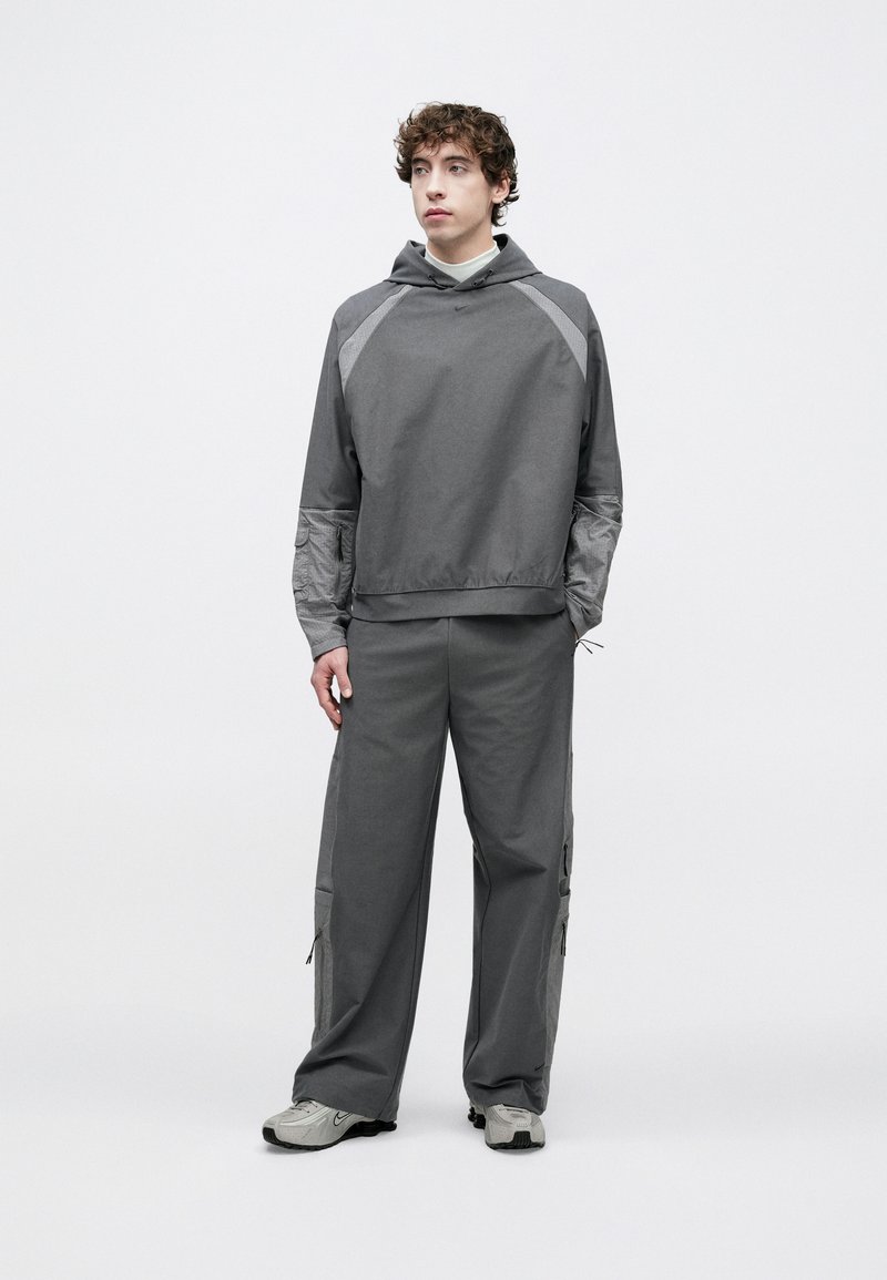 Grå hættetrøje med grå kontrastpaneler, suppleret med matchende grå cargobukser. Stoffets tekstur fremstår glat og let.