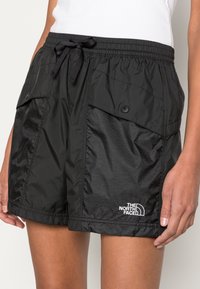 Czarne spodenki wykonane z gładkiego, lekkiego materiału. Posiadają dwie boczne kieszenie zapinane na zatrzaski oraz ściągacz w talii z sznurkiem. Logo umieszczone na dolnym brzegu.