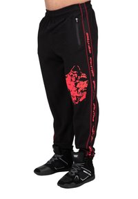 Zwarte gemêleerde sweatpants met een rode gorilla-afbeelding en zijstripe, voorzien van met rits sluitende zakken en zwarte sportieve schoenen.