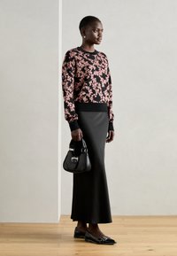 Črna pletenina s cvetličnim vzorcem, črna maksi krila, črne balerinke z okrasnimi detajli in mala črna torbica. Gladke teksture, prilegajoč se videz.