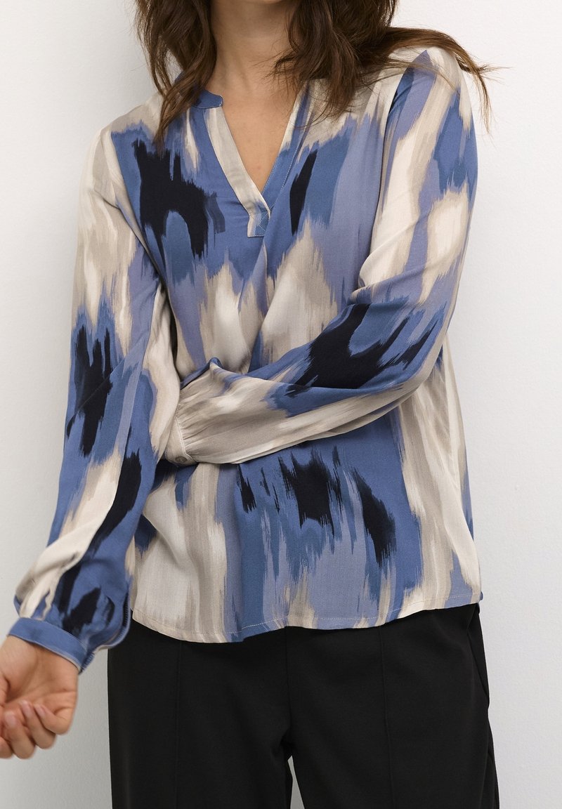 Blouse à manches longues, col en V, en tissu doux avec un motif bleu et beige. Présente un design abstrait de coups de pinceau dans des nuances variées.