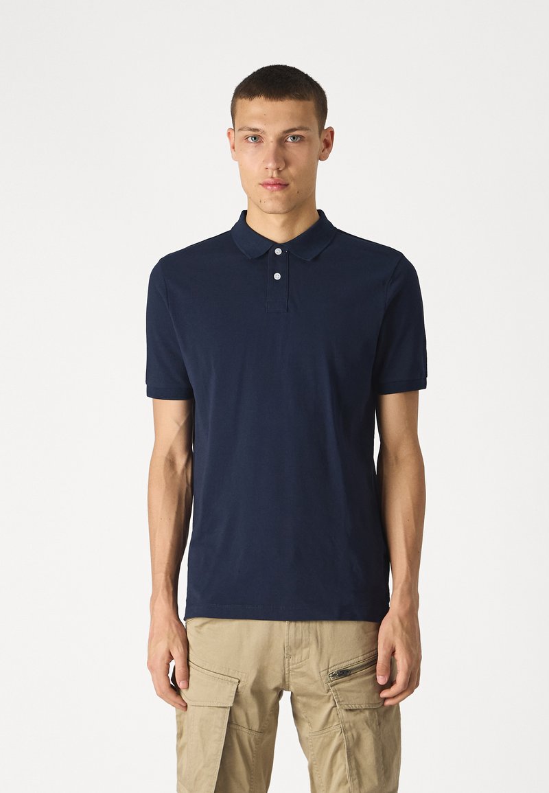 Polo shirt bleu marine en coton, avec un col classique, un plastron à trois boutons et des manches courtes. Texture simple et lisse.