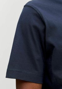 Tume sinine puuvillane T-särk, millel on ringkaelus, lühikesed varrukad ja nähtavad õmblused ääres. Pehme tekstuur ja lihtne disain.