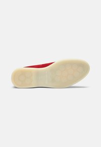 Rode suède schoenzool met een crèmekleurige rubberen buitenzool die is voorzien van ronde grippatronen en een gestructureerd oppervlak voor grip.