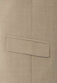Beige stof met een gestructureerd oppervlak, voorzien van een opgenaaide, rechthoekige patchzak aan de rechterzijde, met netjes afgewerkte randen.