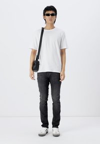 Witte t-shirt met korte mouwen, donkere jeans, zwarte schoudertas, zwarte zonnebril en witte sneakers met grijze accenten; eenvoudig ontwerp en pasvorm.