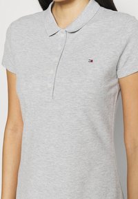 Grijze katoenen poloshirt met een kraag, korte mouwen en een placket met vijf knopen. Bevat een klein geborduurd driekleurig logo op de borst.