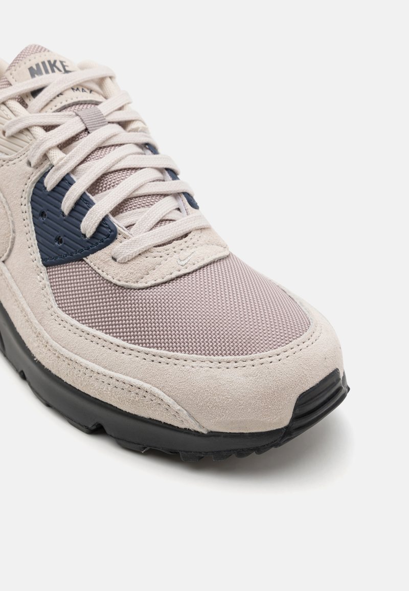 Nike Sneaker aus leicht beigem Wildleder und Netzoberfläche mit marineblauen Akzenten, Gummisohle sowie gepolsterter Zunge und Kragen für zusätzlichen Halt.