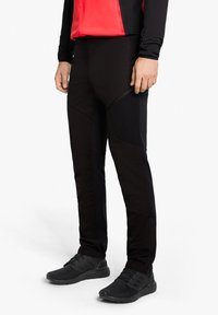 Schwarze Sporthose mit figurnahem Design, ausgestattet mit Reißverschlusstaschen und strukturierten Stoffpaneelen für Atmungsaktivität und Flexibilität.