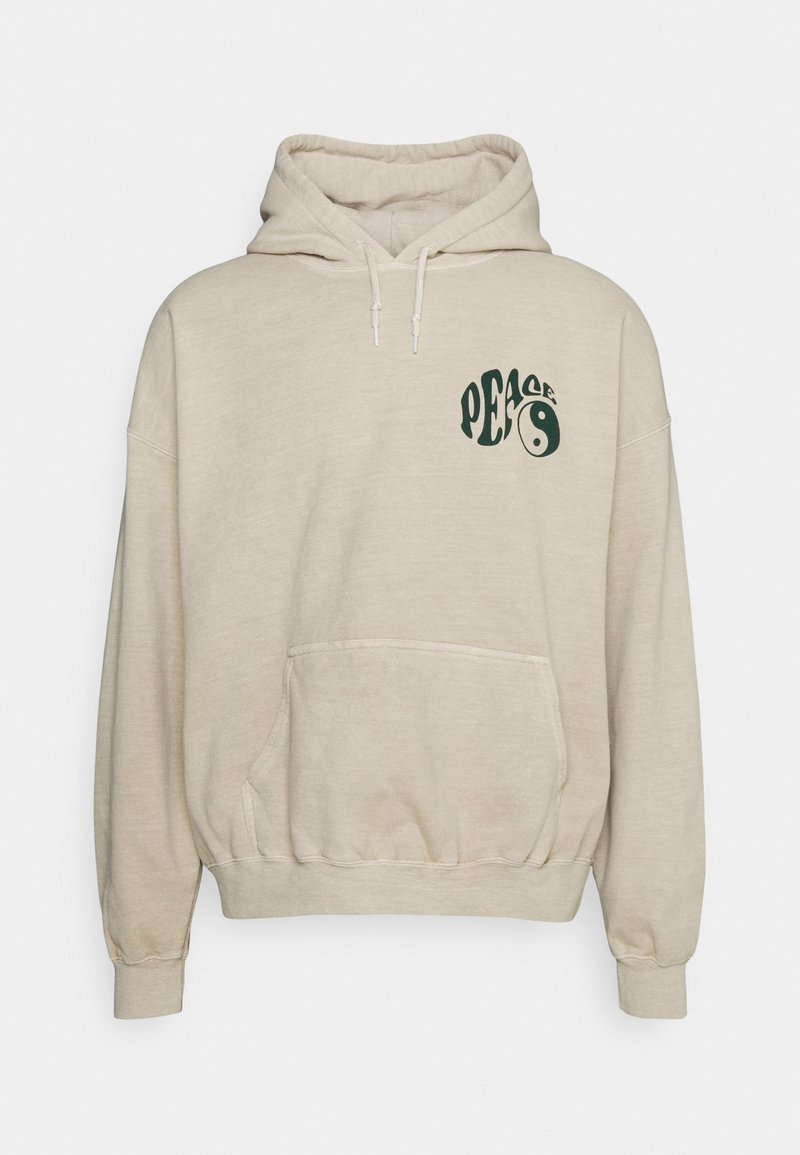 Sudadera beige con bolsillo frontal, capucha y ajuste holgado. Presenta un texto gráfico en verde oscuro que dice "PAZ" con un diseño de yin-yang en el lado izquierdo del pecho.