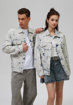 Lichte blauwe spijkerjacks met spetterpatroon, gecombineerd met een witte T-shirt en grijze wijde broek; vrouwelijke model in een spijkerrok.