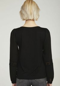 Svart långärmad topp med rund halsringning, texturerad tyg, spetsdetaljer på ärmarna och en avslappnad passform. Bakvy visar en slät design.