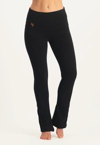 Svarta träningsleggings med en bred, vikbar midja. Slät textur, utsvängda vid fotleden, med en liten broderad logotyp i orange.