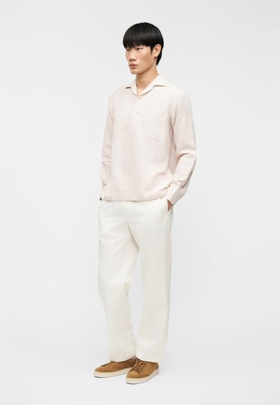 Ροζ ανοιχτόχρωμο πουκάμισο με μακριά μανίκια, γιακά και μπροστινή τσέπη, σε συνδυασμό με άνετο λευκό παντελόνι και καφέ σουέτ παπούτσια. Απλός σχεδιασμός και ουδέτερα χρώματα.