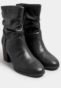 Musta nilkkurit, jotka on valmistettu sileästä nahasta, joissa on löysä muotoilu, sivuvetoketjukiinnitys ja paksu lohkarekorko.