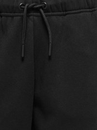 Gros plan de la ceinture d'un pantalon de survêtement noir avec un cordon noir passé à travers des œillets métalliques, montrant la texture du tissu et les détails des coutures.