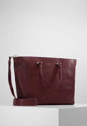 Bordowa torba typu tote ze skóry, z dwoma uchwytami, odpinanym paskiem na ramię oraz małym złotym logo "LYDC London" z przodu.