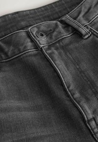 Jeanși negri din denim cu închidere prin nasture, bucle pentru curea și o suprafață texturată cu cusături vizibile de-a lungul cusăturilor.