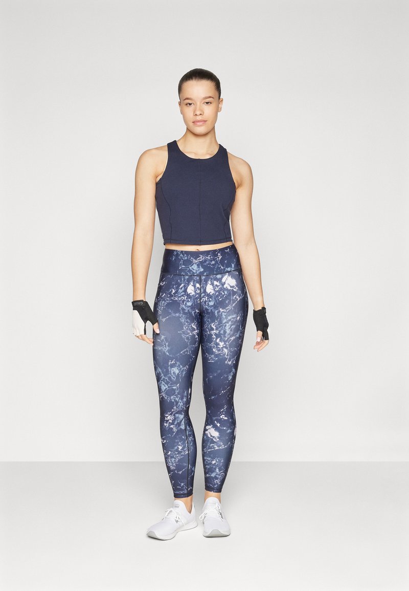 Top corto sport blu scuro e leggings a fantasia nelle tonalità di blu e bianco. Include guanti senza dita e scarpe da uomo bianche.