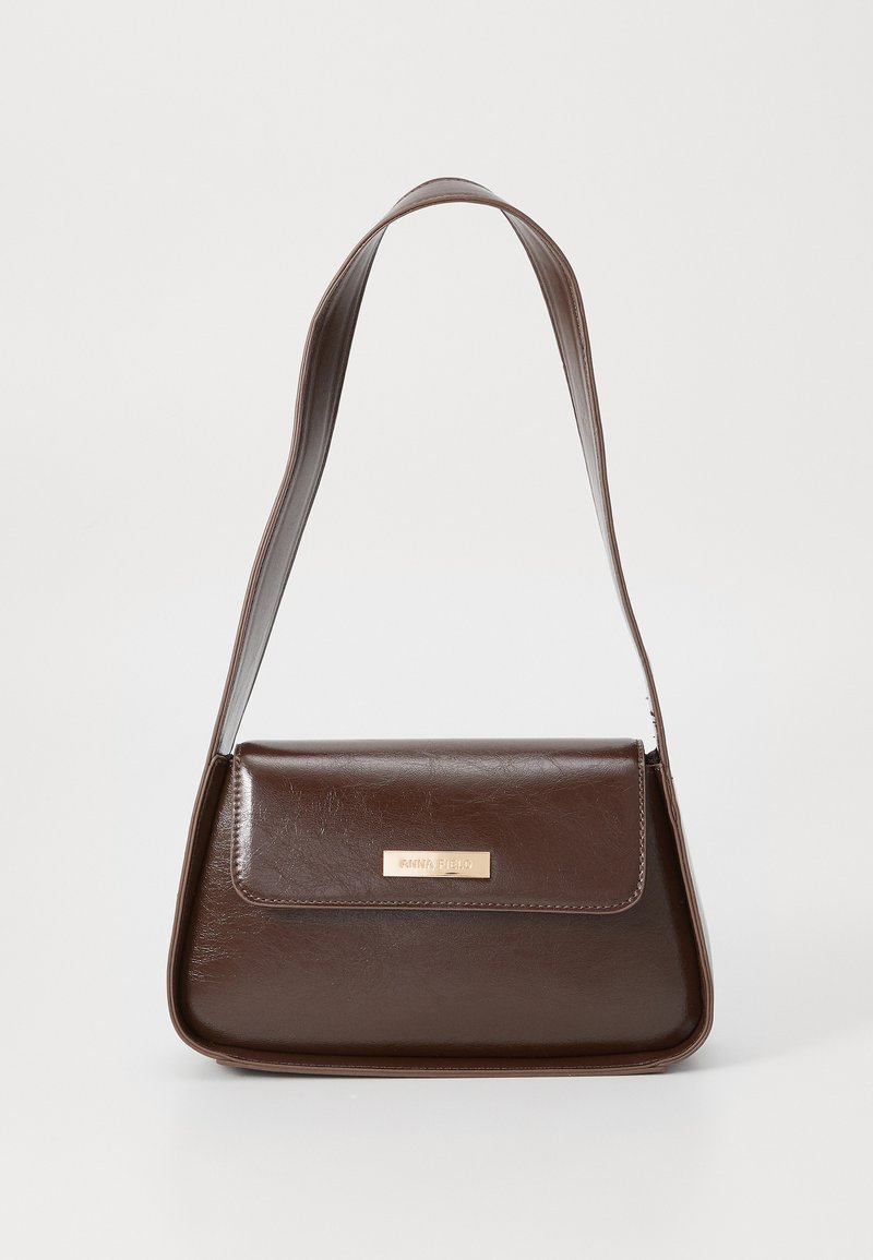 Brown leather shoulder bag with a structured shape, featuring a magnetic flap closure and a metallic logo accent on the front.